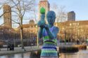 Statue de femme nue portant un enfant, habillée d’une robe rayée en tricot coloré et d’un bonnet vert, dans un parc à Copenhague.