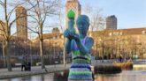 Statue de femme nue portant un enfant, habillée d’une robe rayée en tricot coloré et d’un bonnet vert, dans un parc à Copenhague.