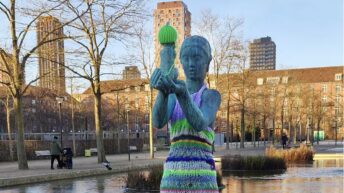 Statue de femme nue portant un enfant, habillée d’une robe rayée en tricot coloré et d’un bonnet vert, dans un parc à Copenhague.