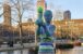 Statue de femme nue portant un enfant, habillée d’une robe rayée en tricot coloré et d’un bonnet vert, dans un parc à Copenhague.